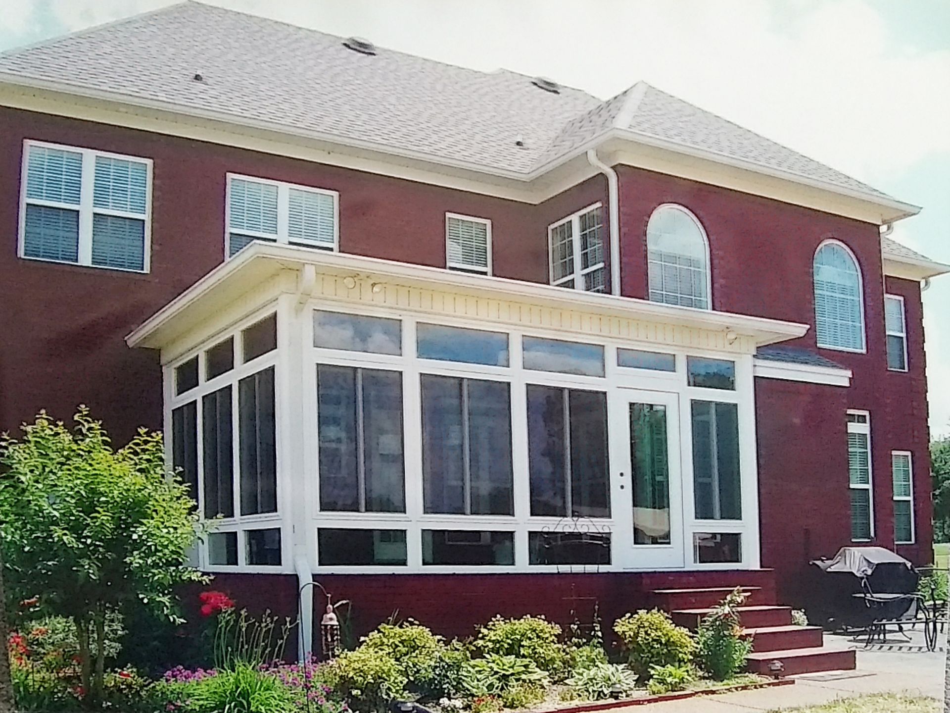 Red brick house with a white-framed screened porch, a grill, and landscaping.
