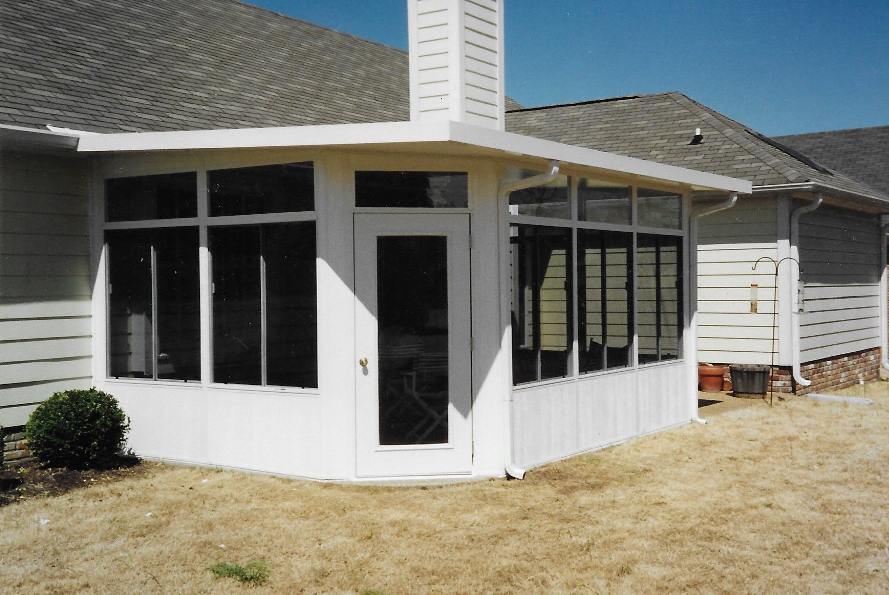 White-walled sunroom with glass windows and a door attached to a house with a chimney.