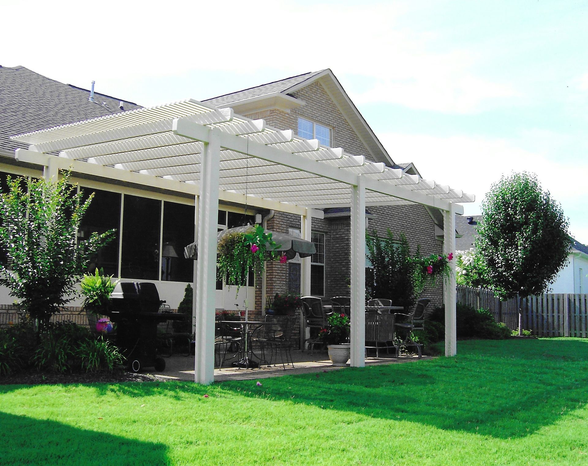 White pergola attached to a house, with green lawn and landscaping.