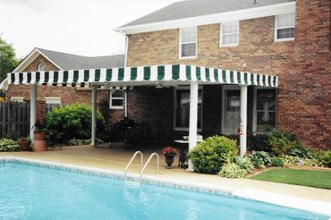 A house with a green and white awning over a swimming pool
