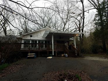 A small white house with a large deck in the middle of a forest