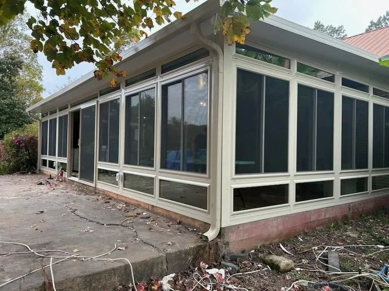 Exterior view of a sunroom with large screened windows and a concrete patio.