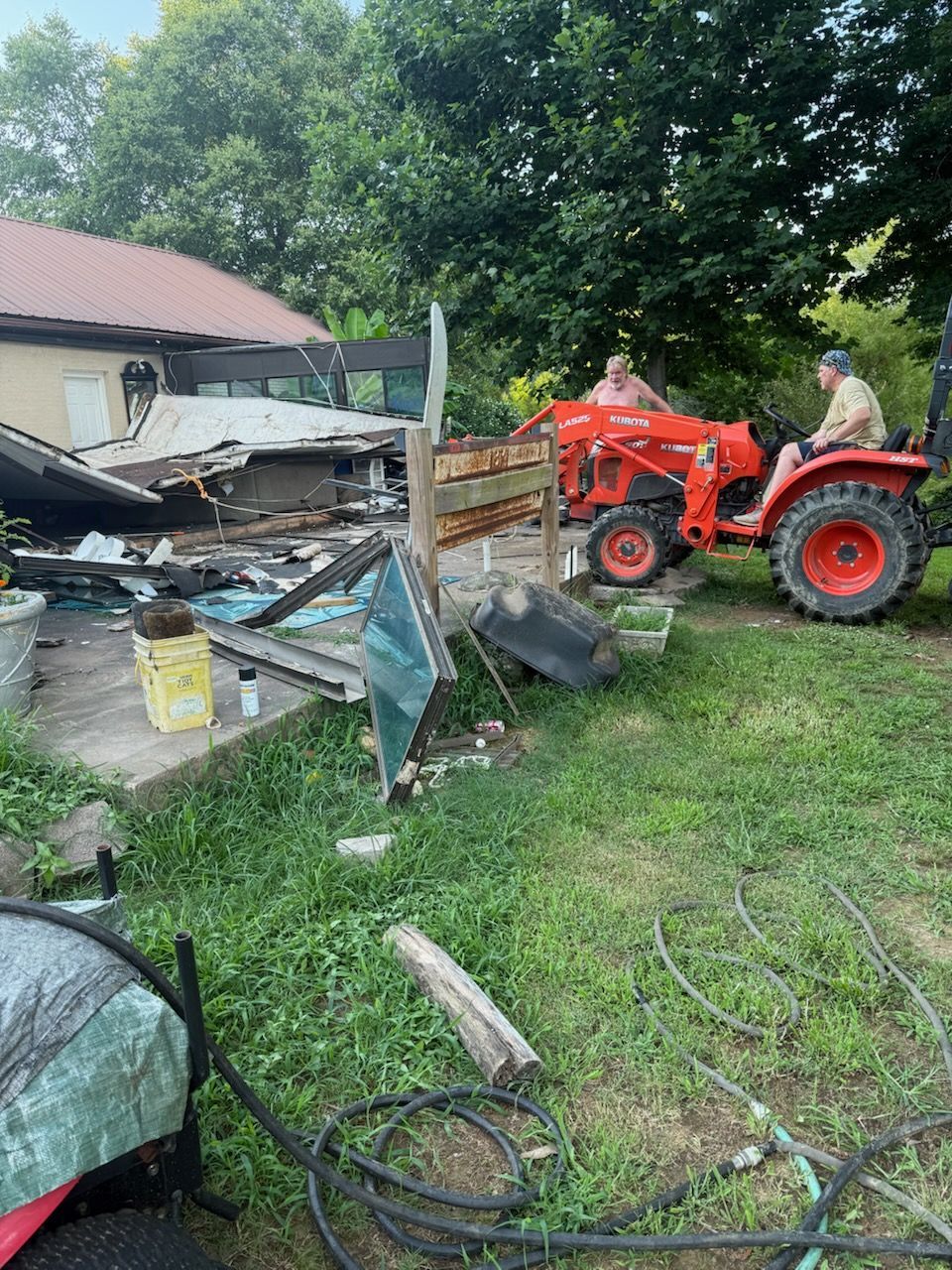 Man operating orange tractor. Debris scattered in yard next to a building.