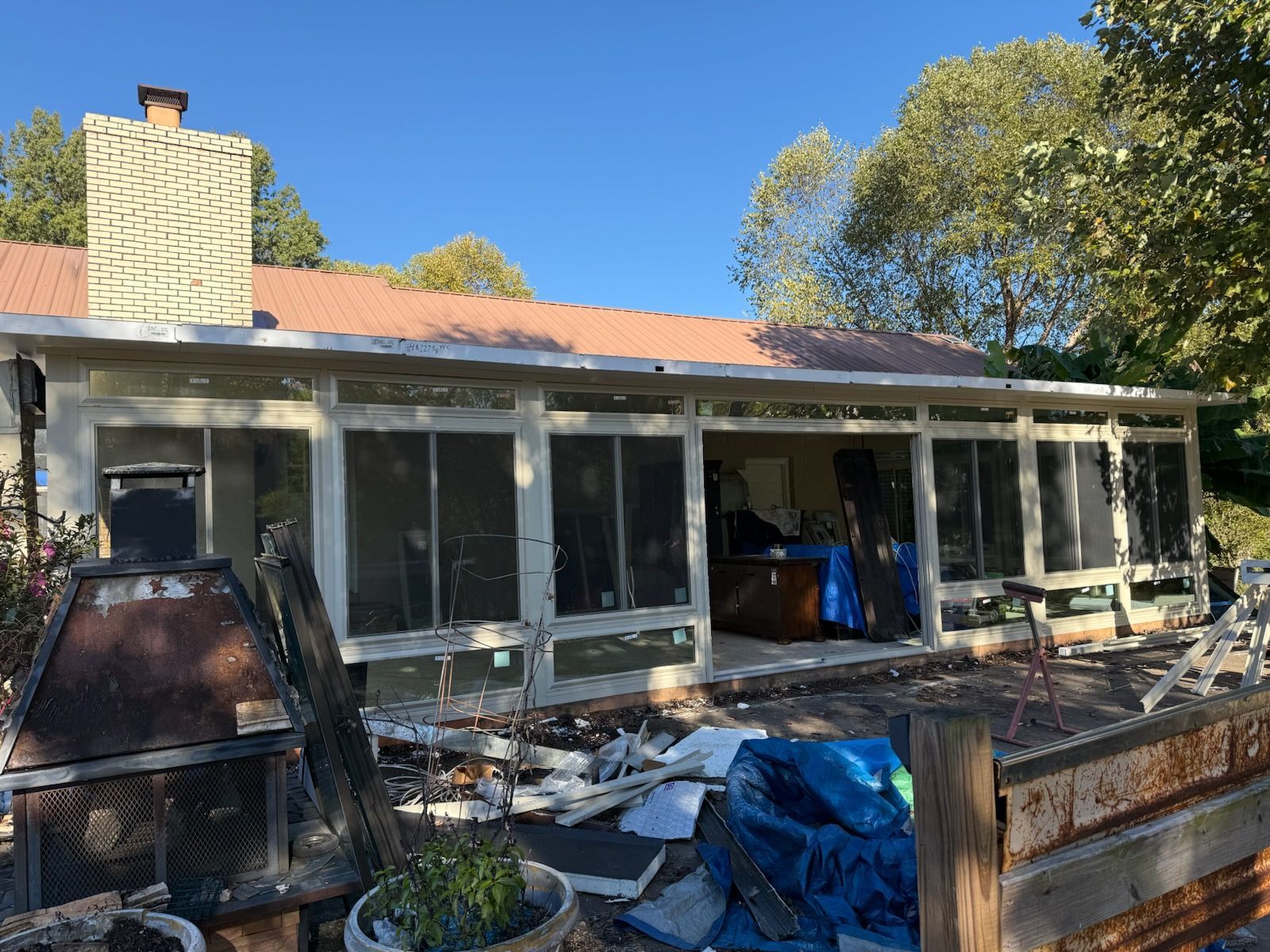 Exterior of a house undergoing renovation, with a porch area, visible debris, and a chimney.