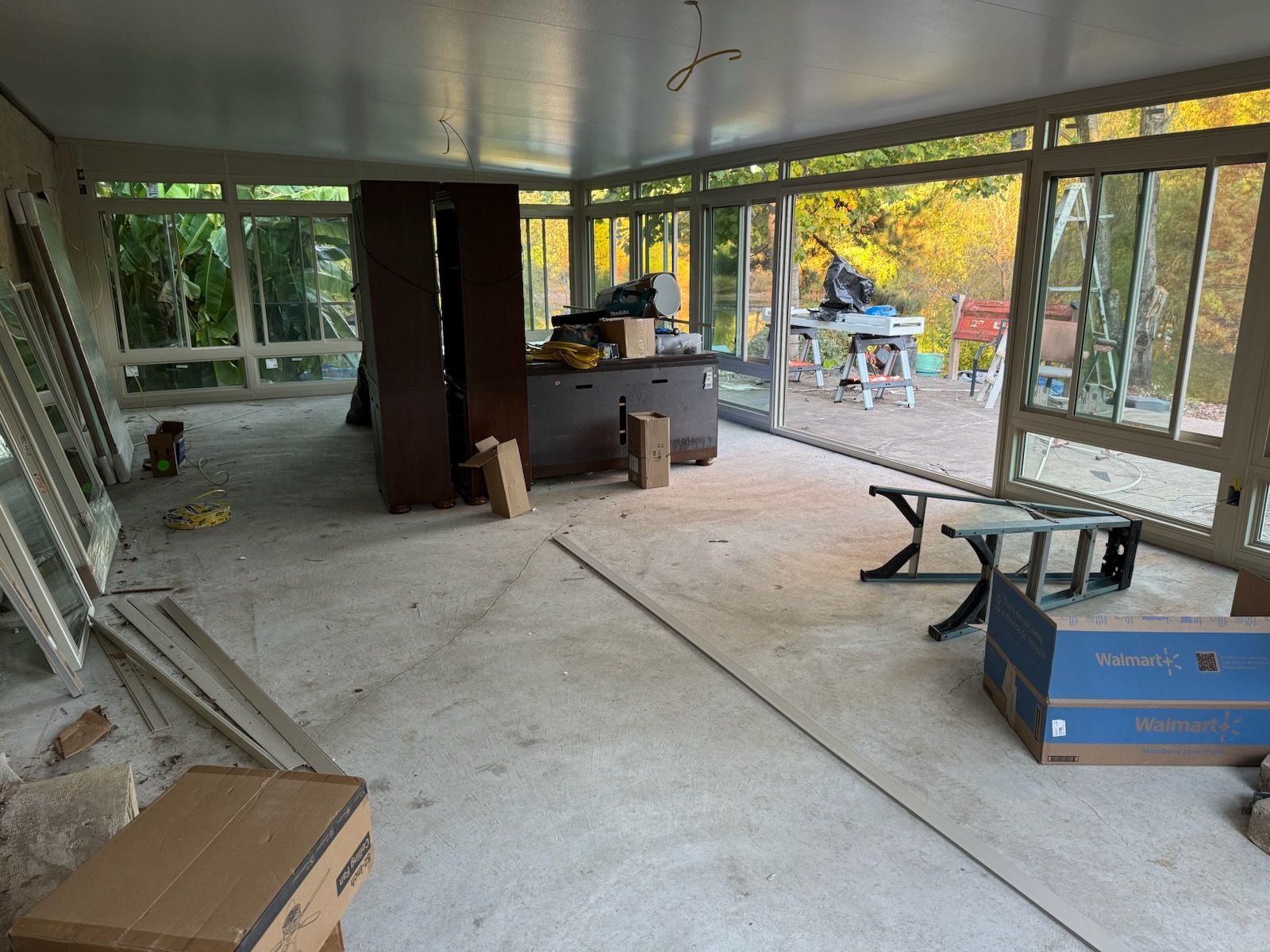 Sunroom under construction with concrete floor, large windows, and unfinished interior.