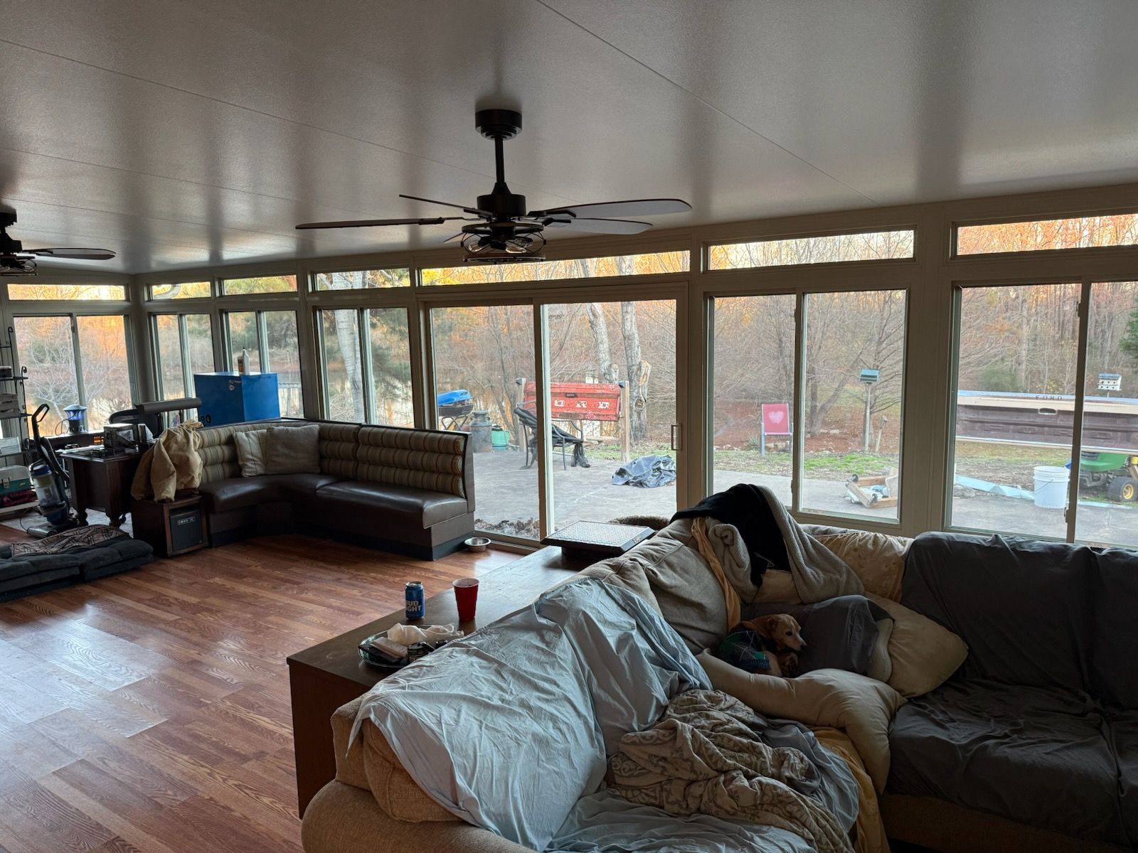 A living room with large windows overlooking trees. A person sleeps on a sofa.