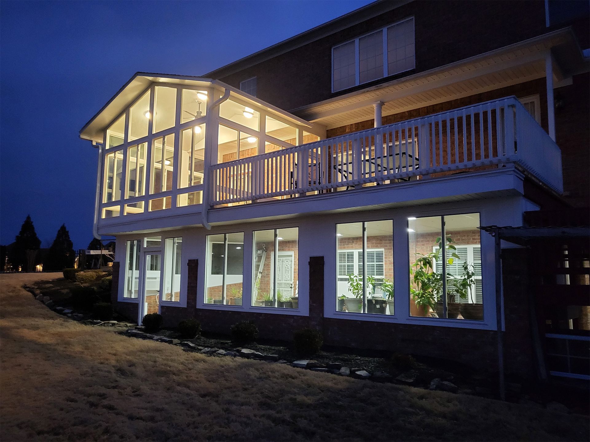 Two-story house with illuminated sunroom and deck at dusk.