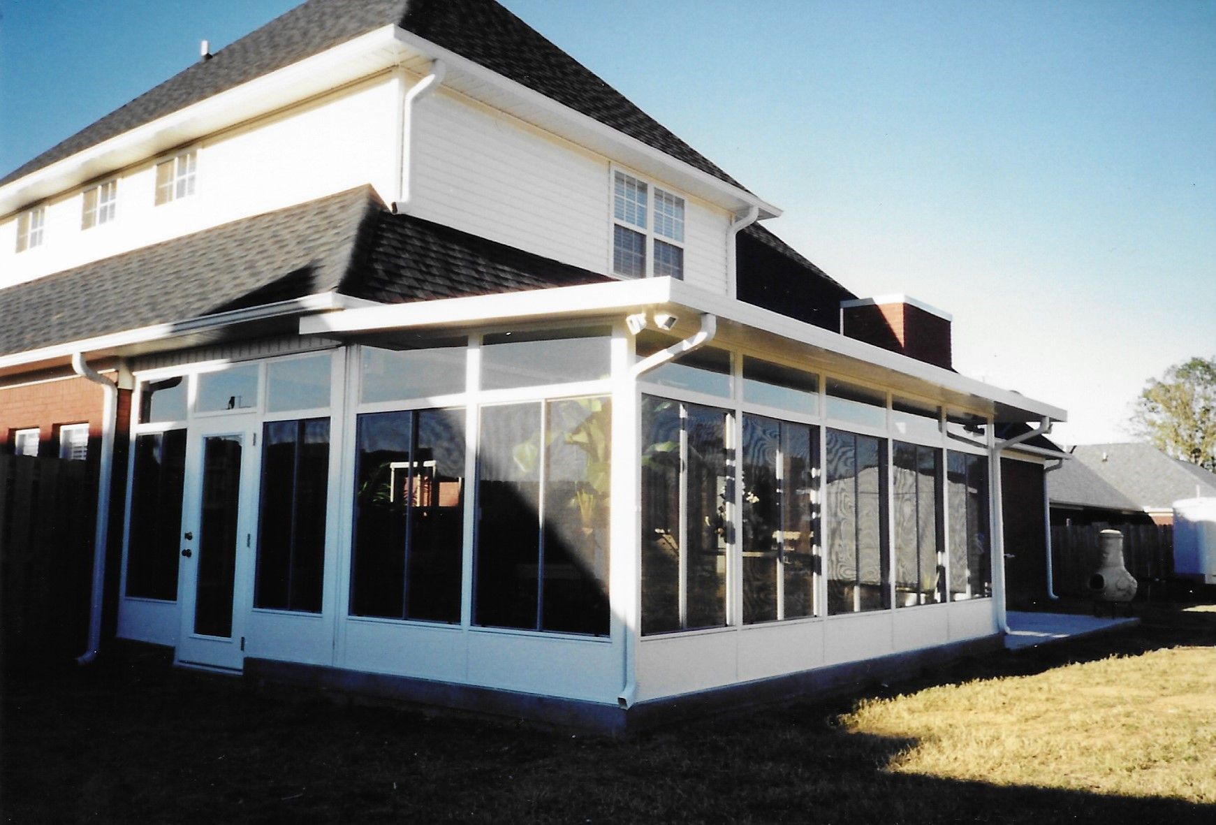 White sunroom attached to a two-story house with dark roof and windows. White sunroom attached to a two-story house with dark roof and windows.