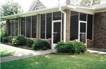 A screened in porch with a brick house in the background