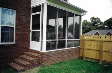 A screened in porch on the side of a brick house