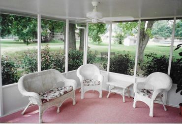 A screened in porch with white furniture and a ceiling fan