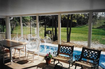 A screened in porch with a table and chairs overlooking a swimming pool.