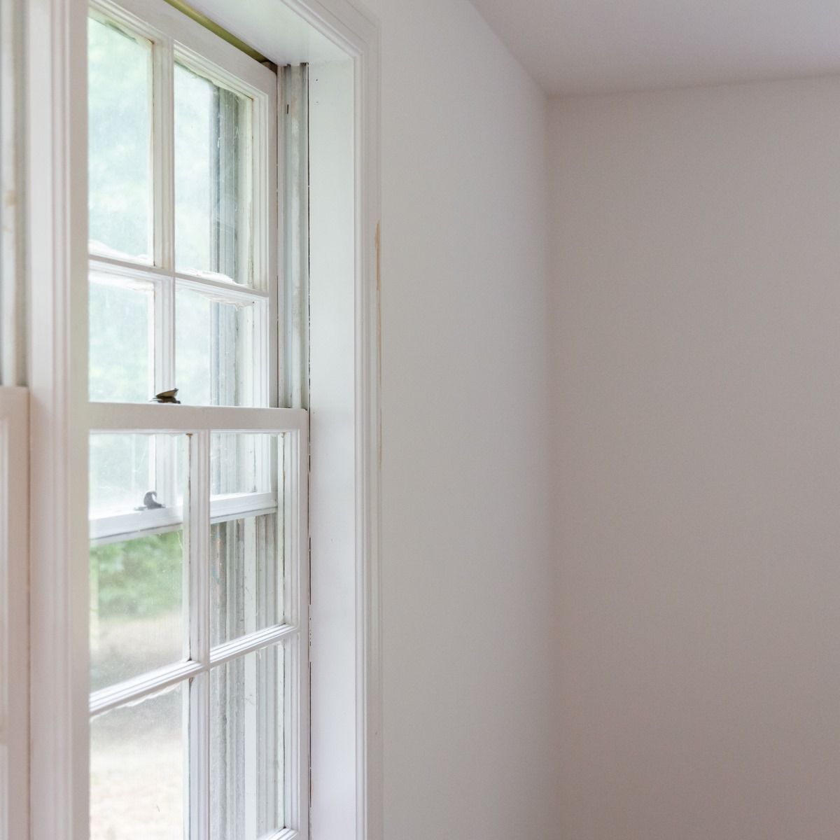 There is a window in the corner of a room with white walls.