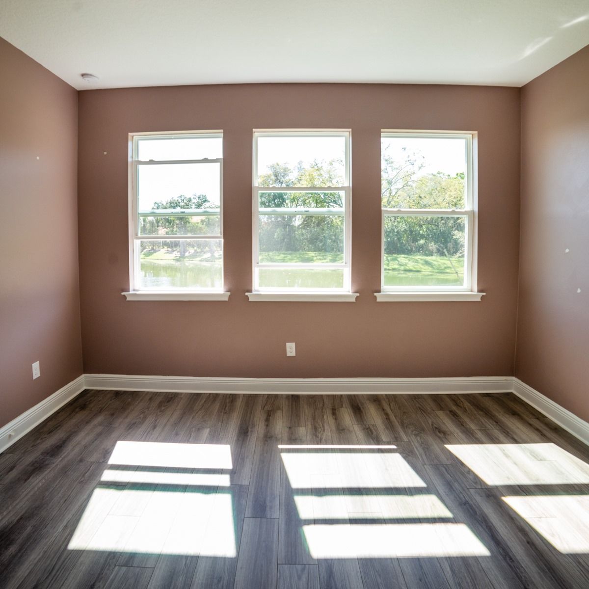 An empty room with three windows and a wooden floor.