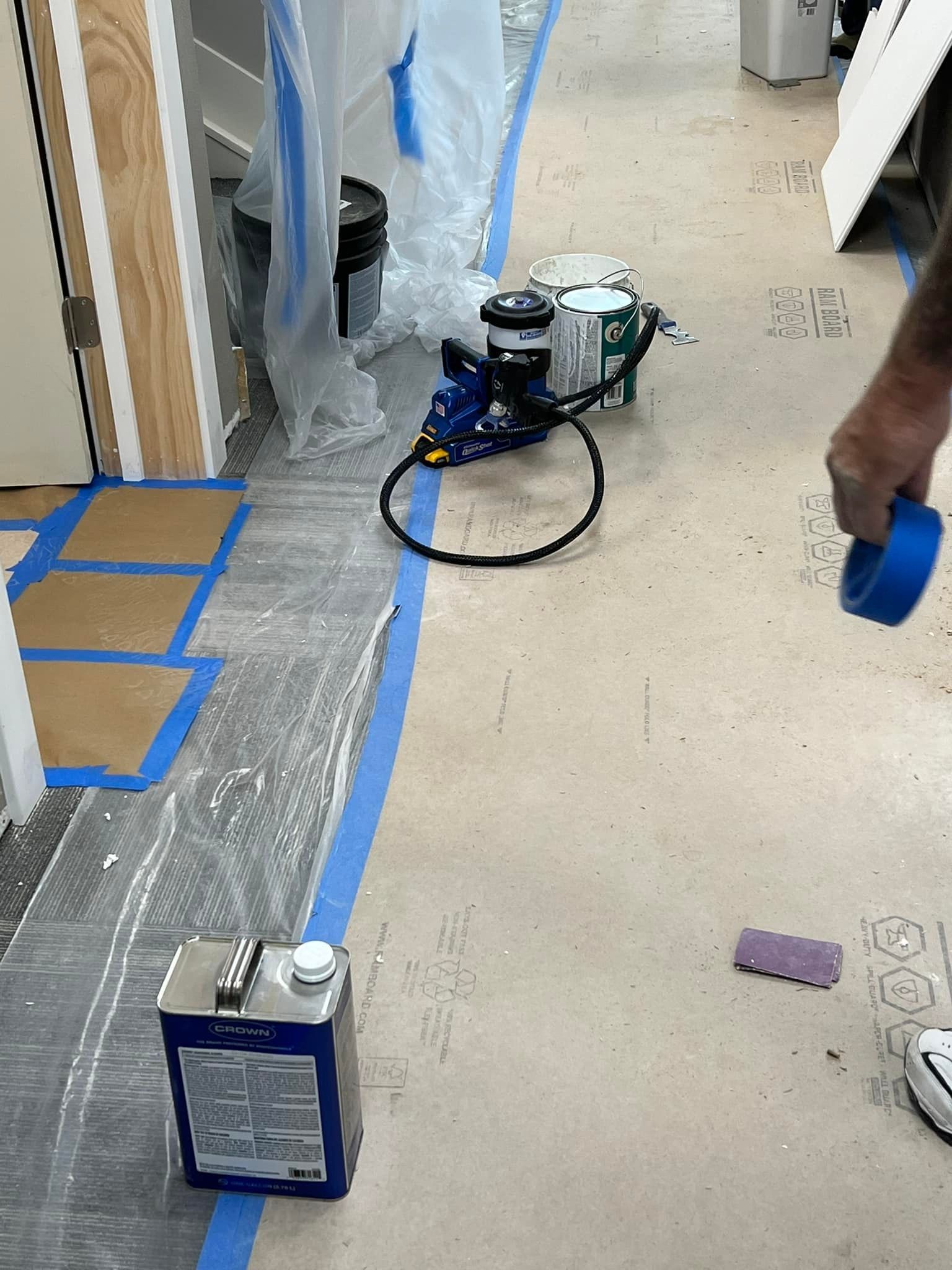 A person is holding a can of blue tape on the floor.
