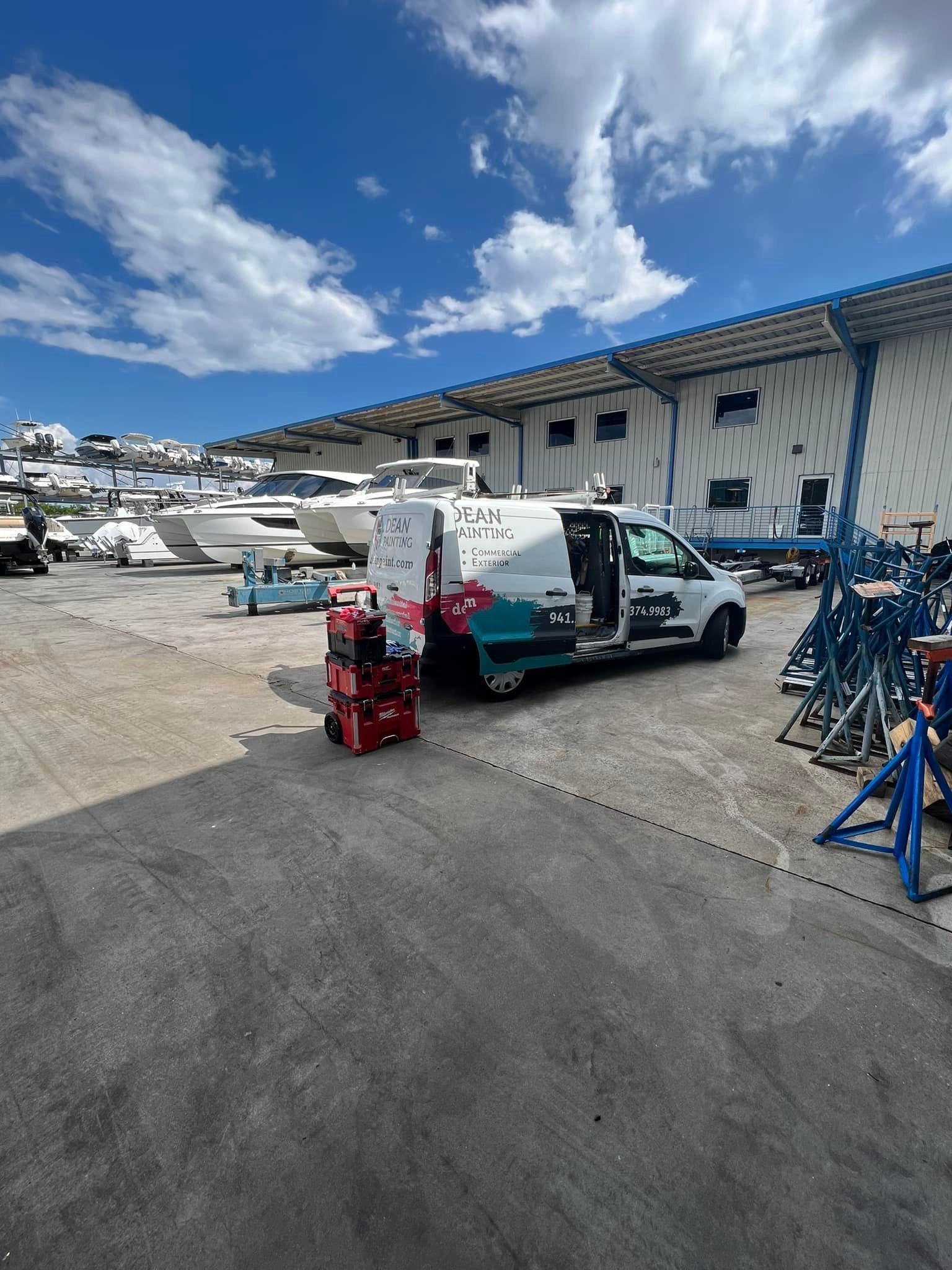 A white van is parked in a parking lot with boats in the background.