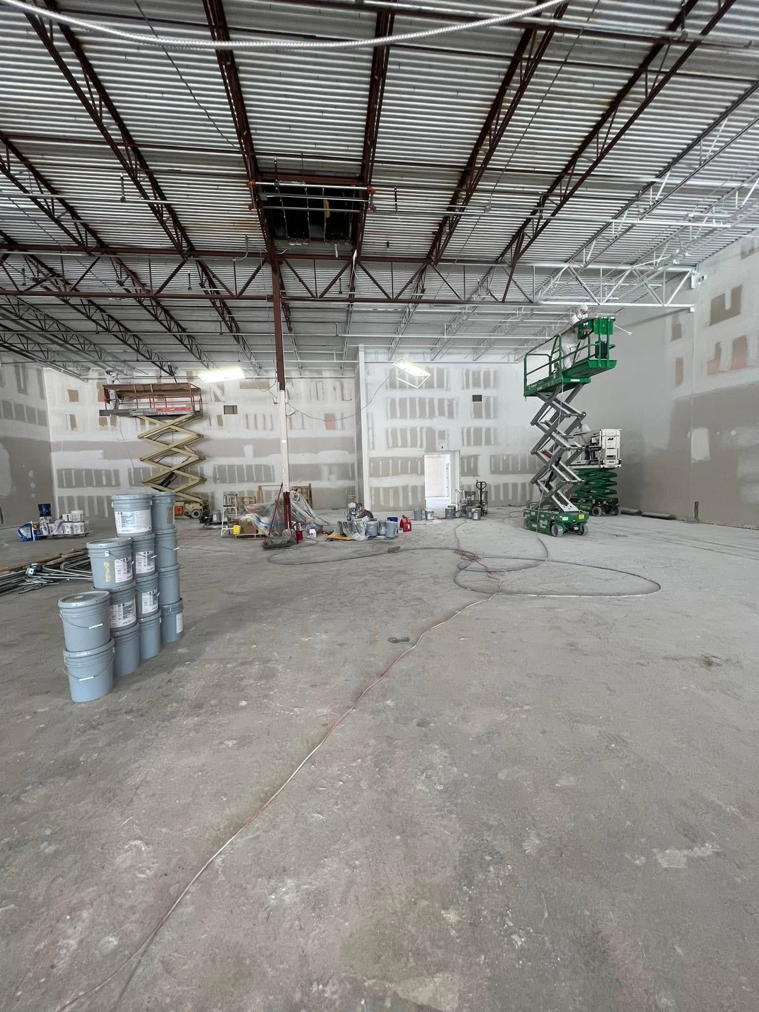 An empty warehouse with buckets of paint and a scissor lift.