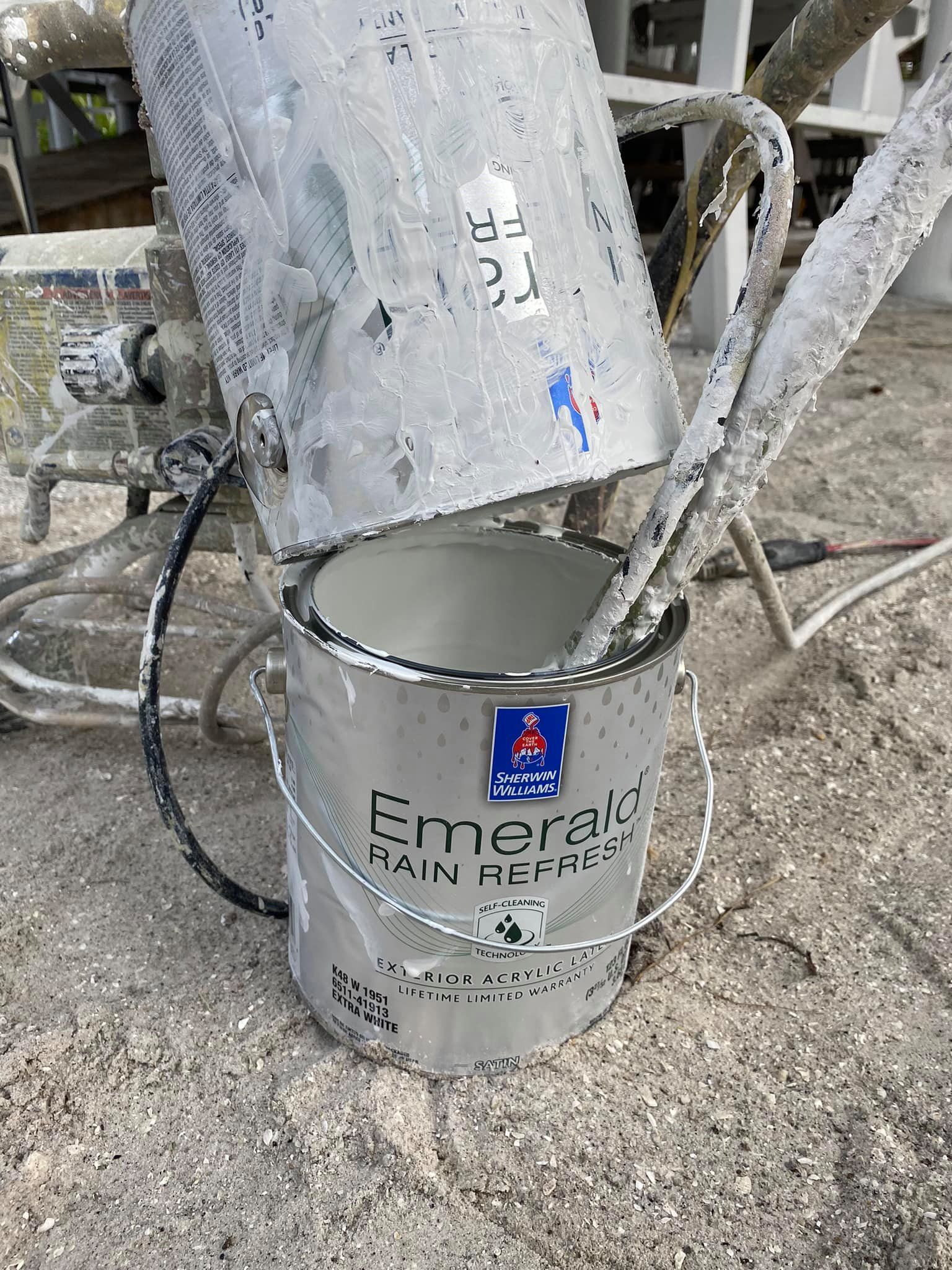 A bucket of paint is sitting on the ground next to a paint sprayer.