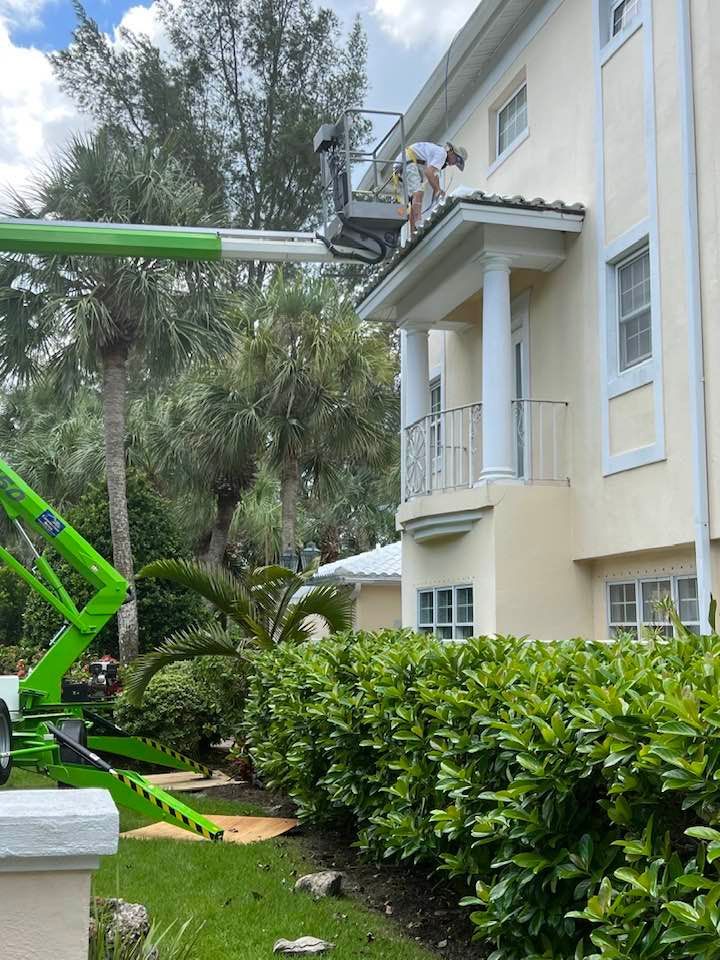 A man is painting the roof of a house with a green crane.