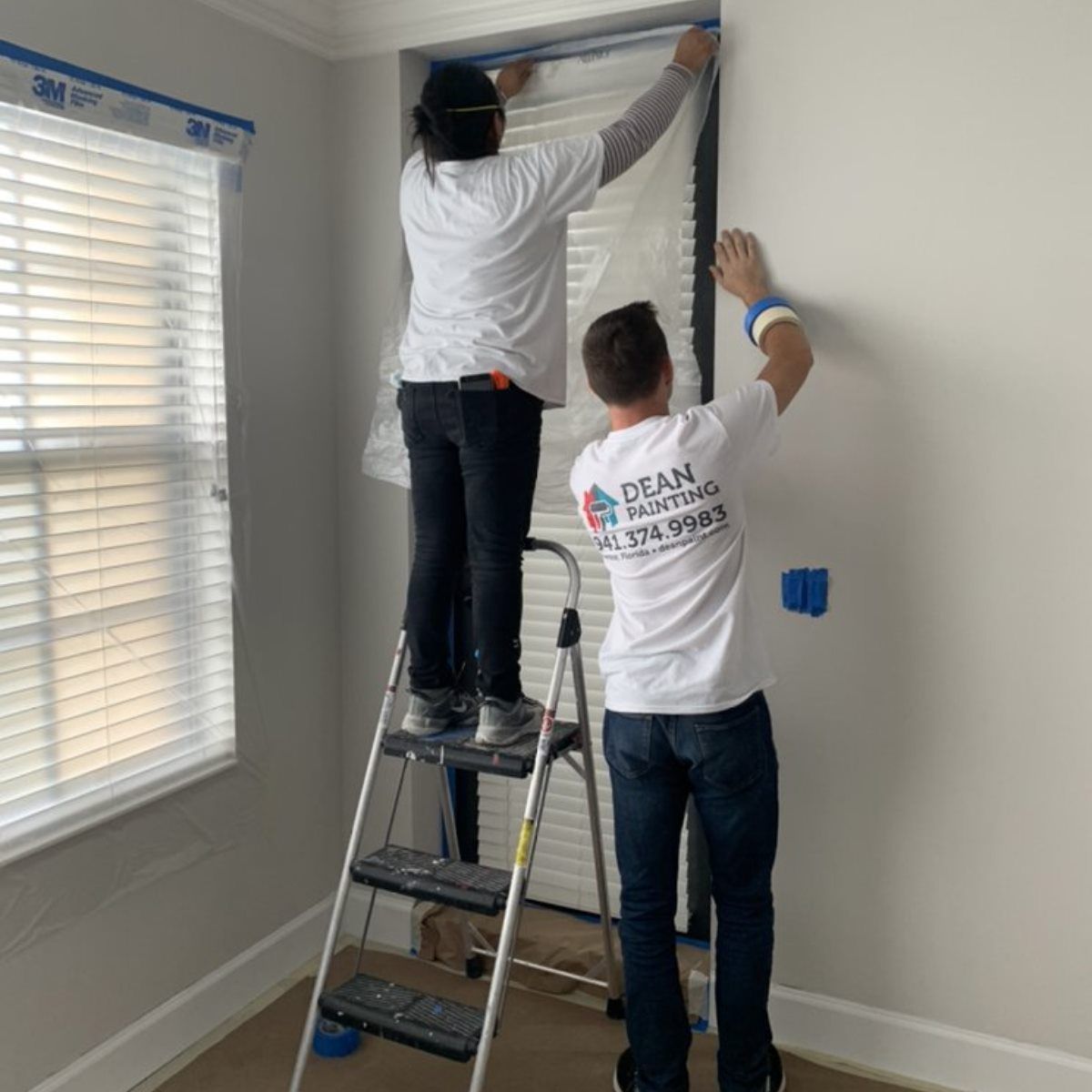 A man and a woman are standing on a ladder in a room.