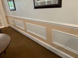 A long hallway with a table , chairs , and pictures on the wall.