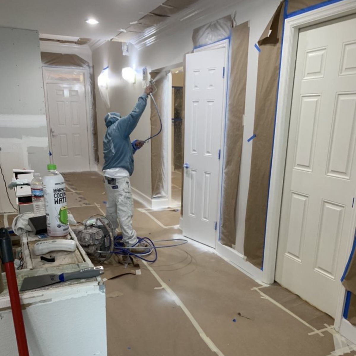 A man is painting a wall in a hallway with a sprayer