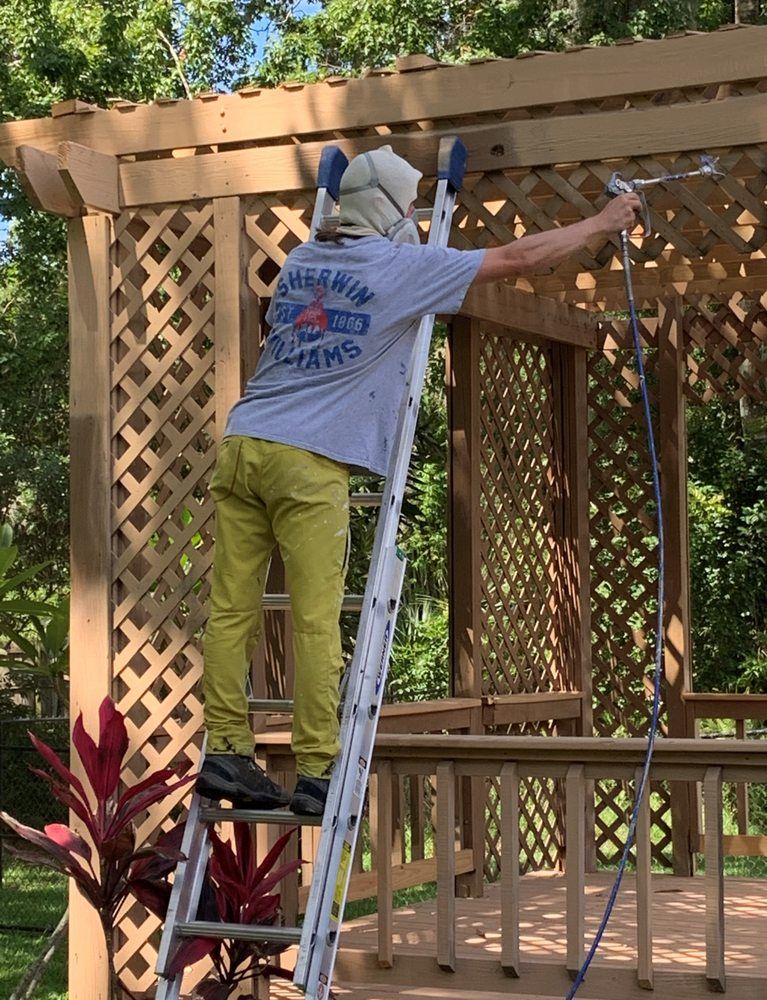 A man is standing on a ladder painting a wooden structure.