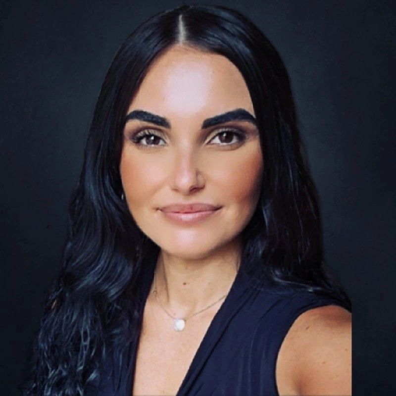 A woman wearing a white jacket and a black turtleneck smiles for the camera.