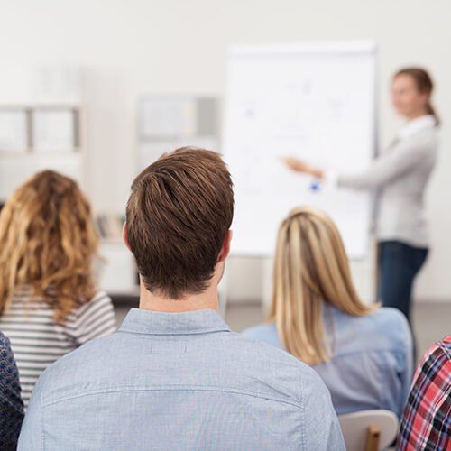 A group of people are sitting in a classroom listening to a presentation.