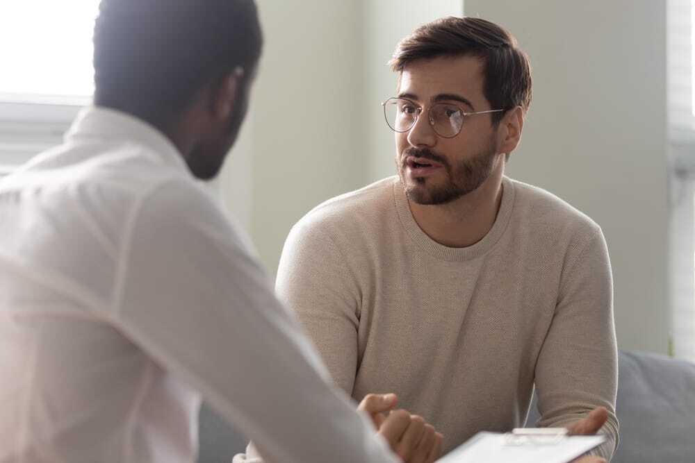 A man is talking to another man while holding a clipboard.