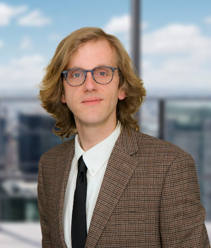 A man wearing glasses and a suit is standing in front of a window.