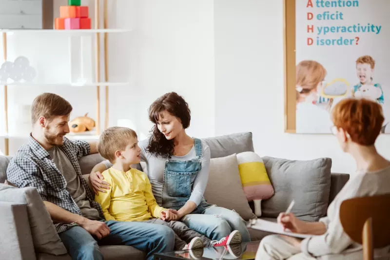 A family is sitting on a couch talking to a woman.