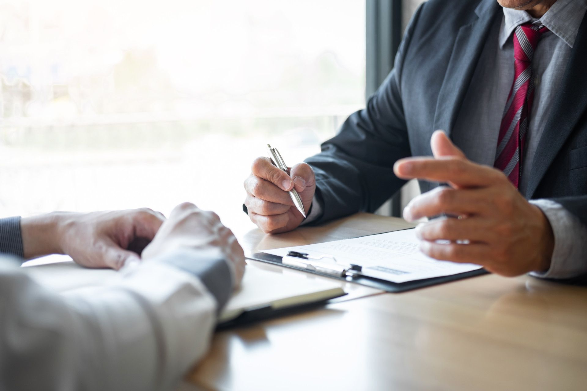 Two people at a desk during a job interview, one holding a pen and gesturing while reviewing a resume.
