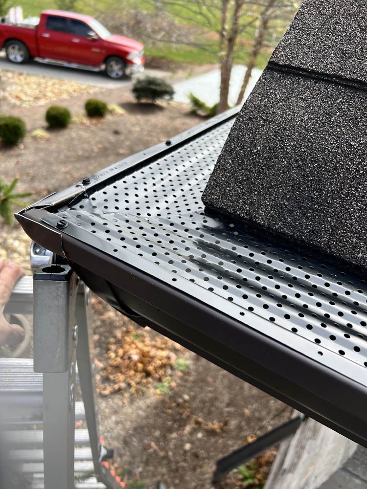 A close up of a gutter on a roof with a red truck in the background.