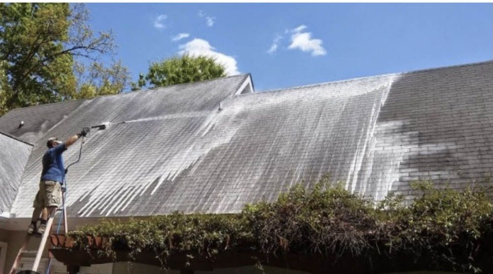 A man on a ladder is cleaning the roof of a house