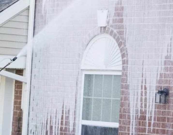 A person is cleaning a brick house with a high pressure washer.