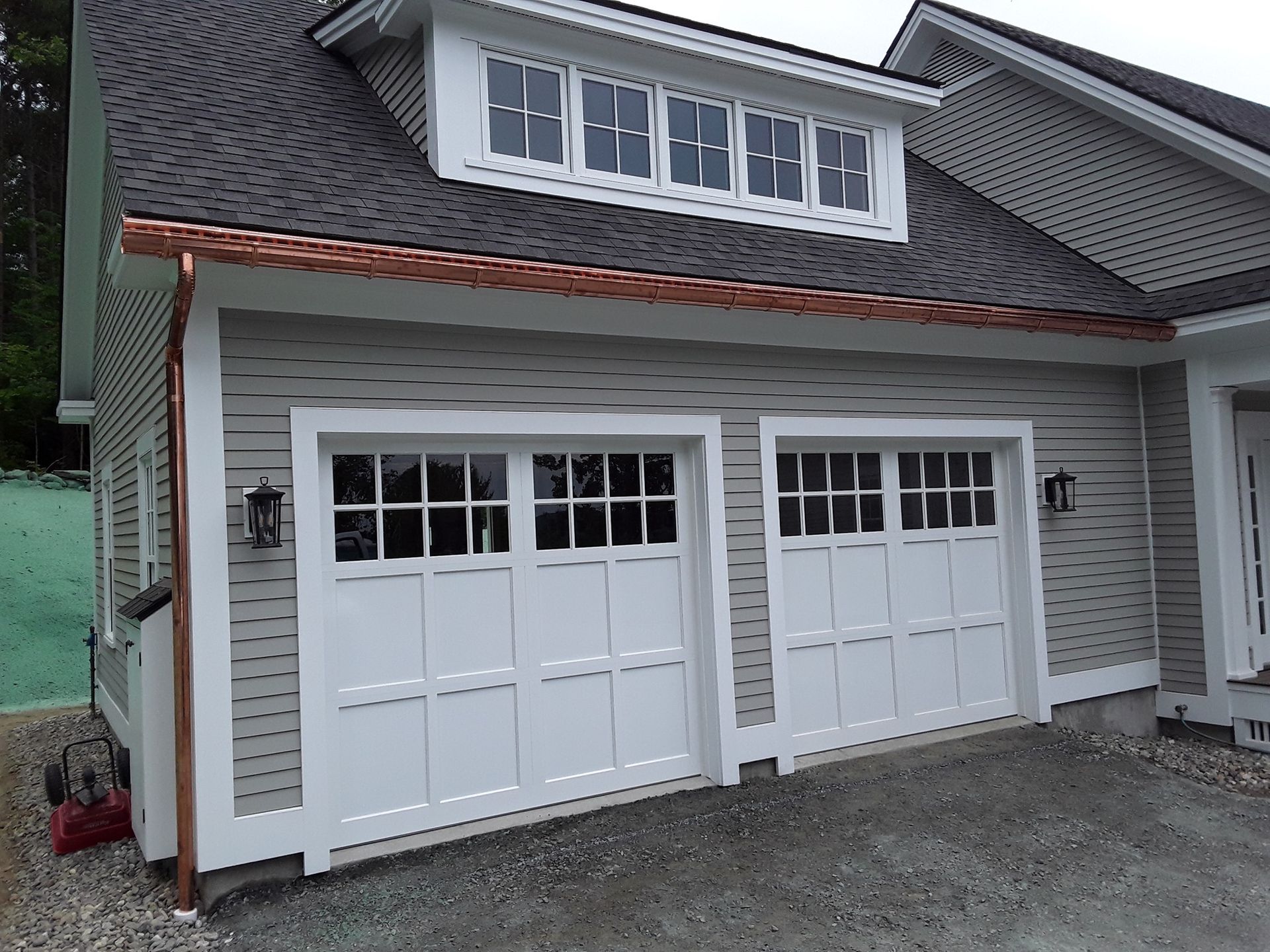 A garage with two white garage doors and a copper gutter
