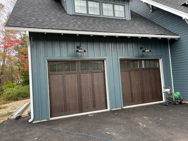 A blue house with two brown garage doors, white seamless rain gutters and a bicycle parked in front of it.