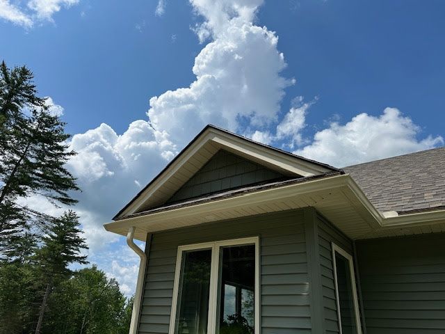 A green house with white seamless rain gutters, a blue sky and white clouds behind it