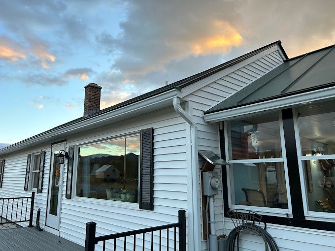 A white house with white seamless rain gutters, black shutters and a large window.