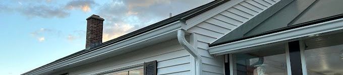 A white house with white seamless rain gutters and a chimney on the roof.