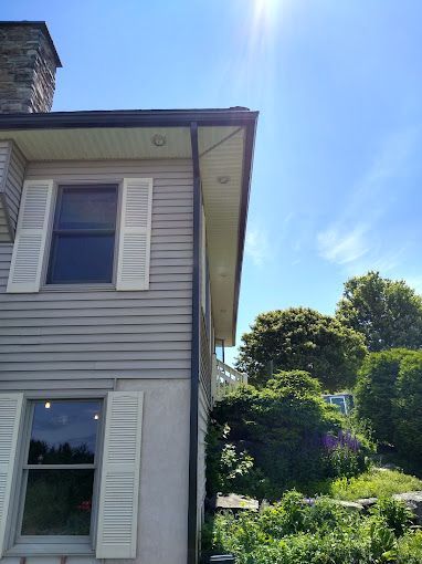 The side of a house with white shutters, black seamless rain gutters and a chimney.