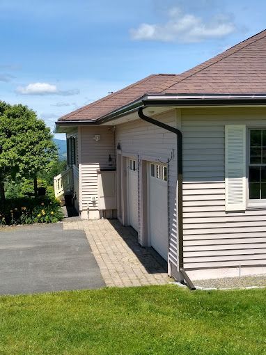 A house with brown seamless rain gutters, and two garage doors and a driveway in front of it.