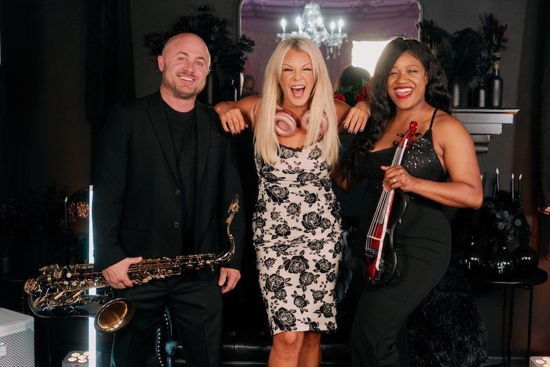 A man is holding a saxophone and two women are holding violins.