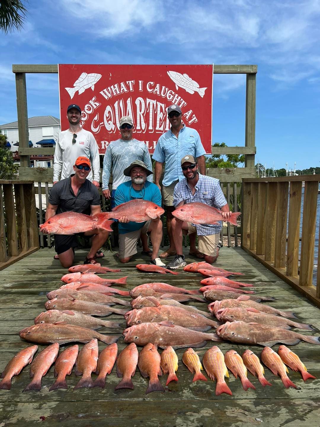 A group of men are standing on a dock holding large fish.