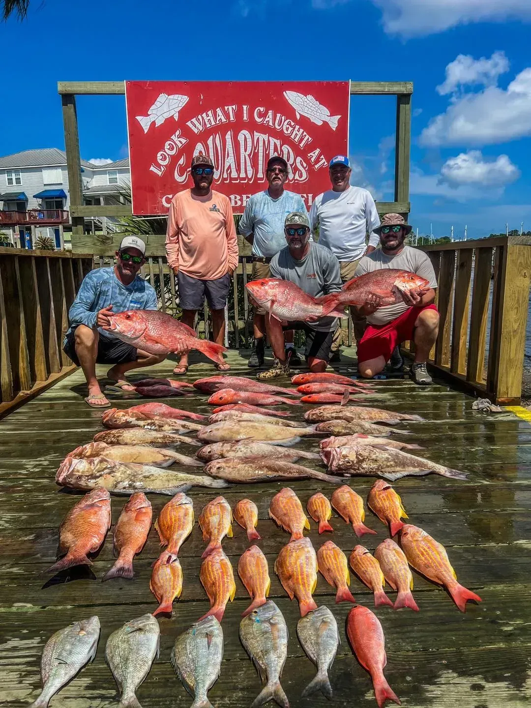 A group of men are posing for a picture with their catch of fish on a dock.