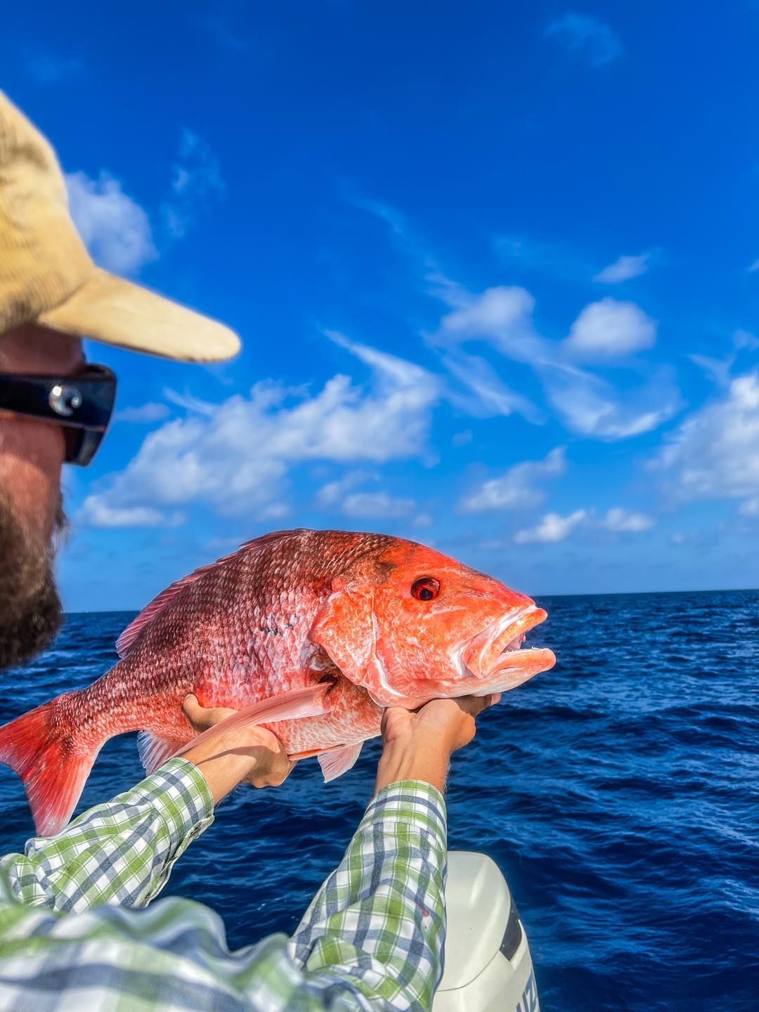 A man is holding a large red fish in his hands on a boat.