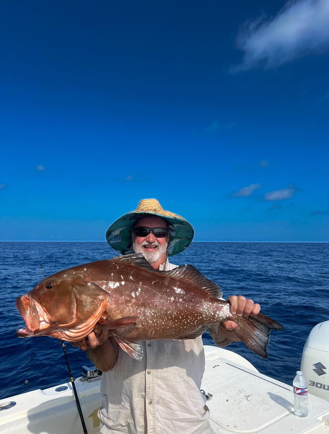 A man is holding a large fish on a boat in the ocean.