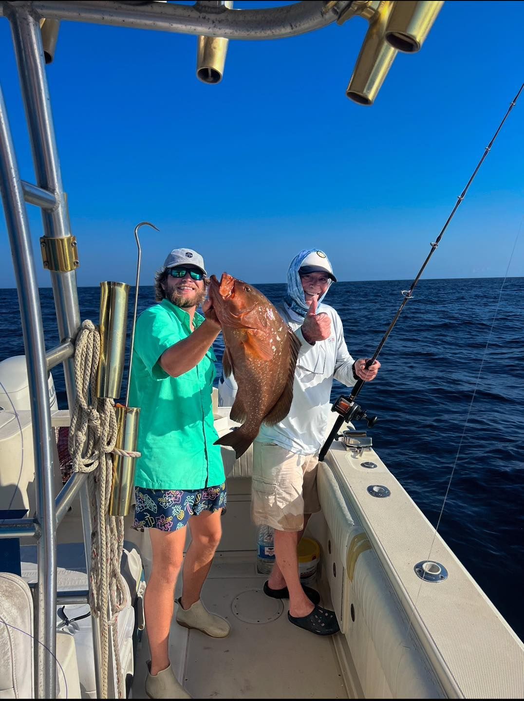 Two men are fishing on a boat and one of them is holding a large fish.