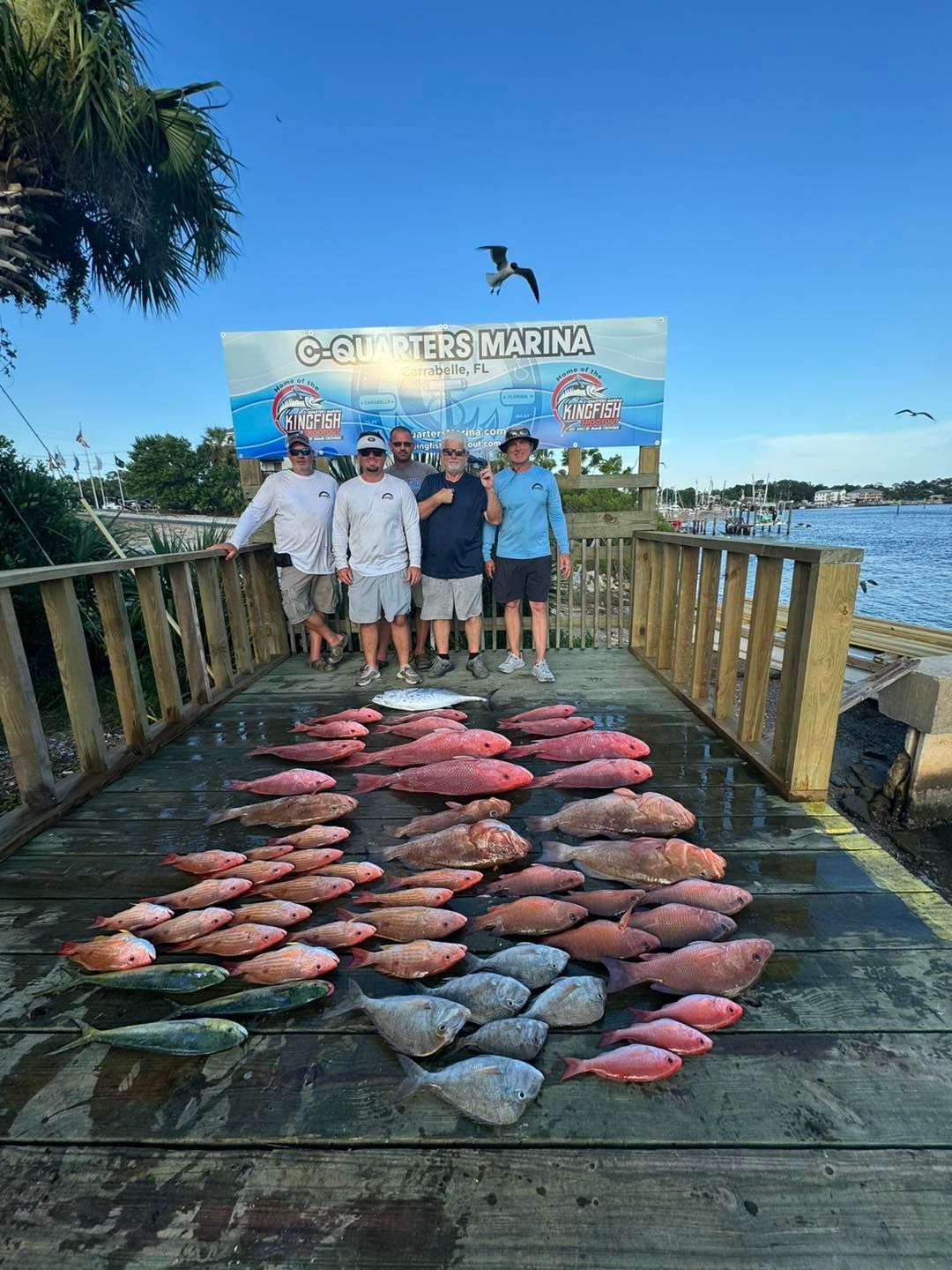 A group of men are standing on a dock with a bunch of fish on it.